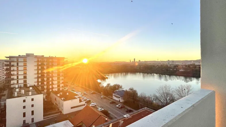Spektakulärer Sonnenaufgang über einem See mit Stadtblick von einem Balkon.