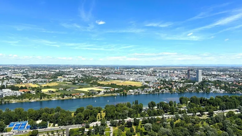 Luftaufnahme der Stadt mit einem breiten Fluss, ausgedehnten Grünflächen und städtischer Bebauung.
