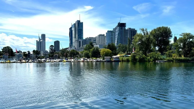 Stadtpanorama mit modernen Gebäuden am Ufer eines Gewässers unter blauem Himmel.