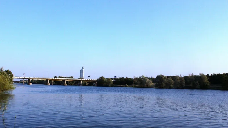 Ruhige Flusslandschaft mit einer Brücke und einem markanten Gebäude am Horizont unter klarem Himmel.
