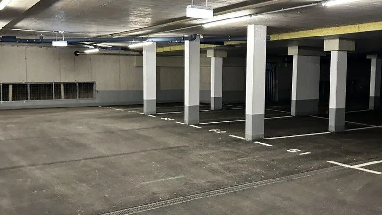 Geräumige Tiefgarage mit vielen leeren Stellplätzen, Betonpfeilern und Deckenbeleuchtung.