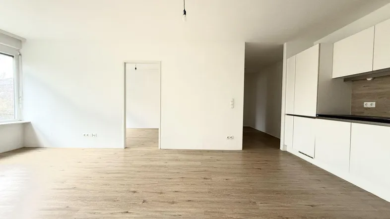 Heller offener Wohnbereich mit integrierter Küche und modernem Laminatboden, ideal für geselliges Beisammensein.