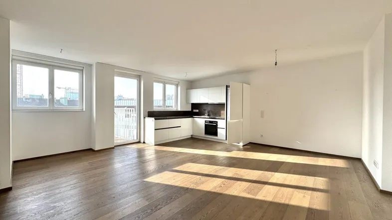 Helles, offenes Wohnzimmer mit integrierter Küche, Holzboden und Zugang zum Balkon.