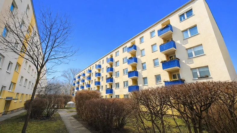 Mehrstöckiges Wohngebäude mit gelb-beiger Fassade und auffälligen blauen Balkonen unter blauem Himmel.
