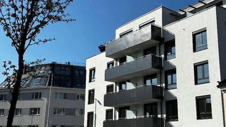 Modernes Wohngebäude mit Balkonen an einer städtischen Straße unter blauem Himmel.