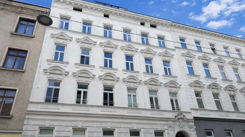 Elegante weiße Fassade eines Altbaus mit vielen Fenstern unter blauem Himmel.