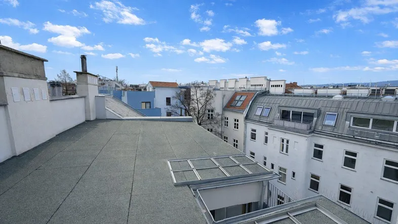 Blick über die Dächer der Stadt mit einem Flachdach und umliegenden Gebäuden unter blauem Himmel.