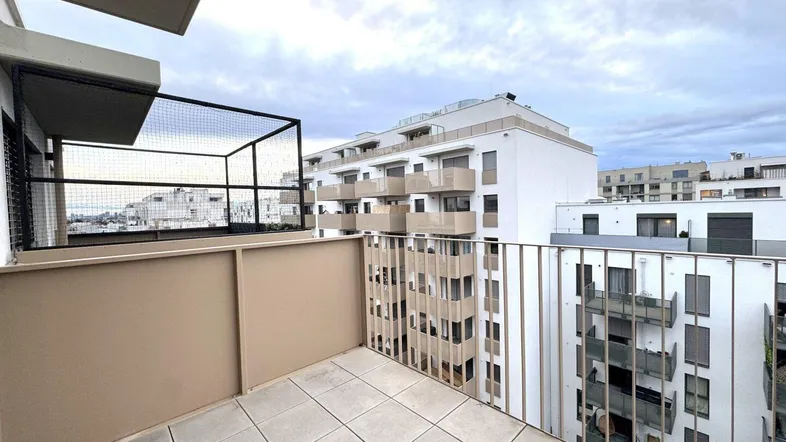 Geräumiger Balkon mit Fliesenboden und Metallgeländer, bietet Blick auf moderne Wohngebäude.