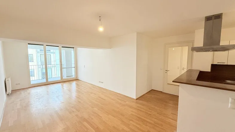 Heller offener Wohnbereich mit Parkettboden und Zugang zu einem Balkon, ideal für modernes Wohnen.