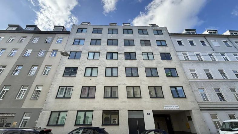 Fassade eines Mehrfamilienhauses mit vielen Fenstern und einem Eingangsbereich auf Straßenniveau.