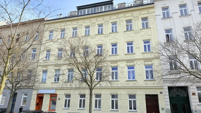 Historisches Gebäude mit gelber Fassade und vielen Fenstern an einer städtischen Straße.