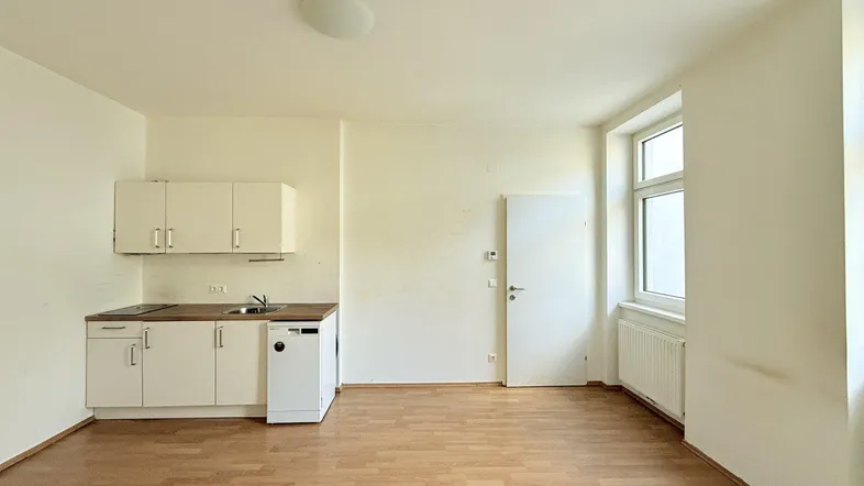 Helles Zimmer mit integrierter Küchenzeile, Laminatboden und einem Fenster für natürliches Licht.