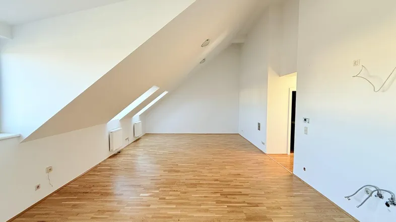 Heller Dachgeschossraum mit Holzboden, schrägen Wänden und Dachfenstern, ideal als Wohnbereich.