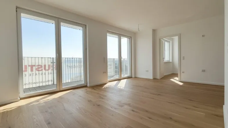 Helles, leeres Wohnzimmer mit Holzboden und Zugang zu einem Balkon, bereit zum Einzug.