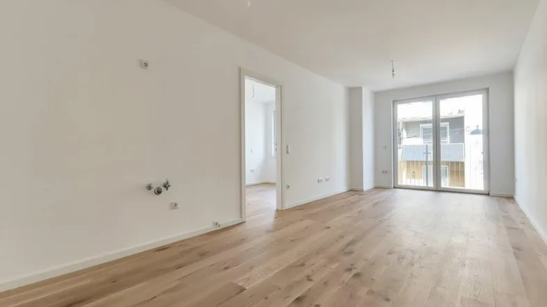Helles, leeres Zimmer mit Holzboden und Zugang zu einem französischen Balkon.