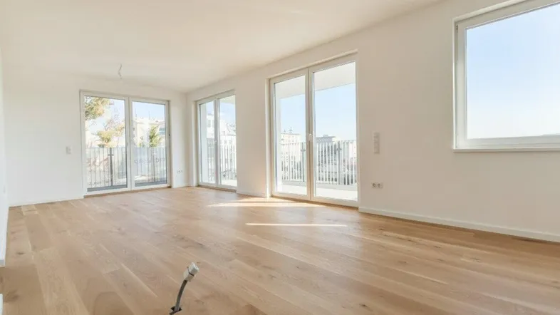 Helles, leeres Wohnzimmer mit modernem Holzboden und Zugang zu einem Balkon.