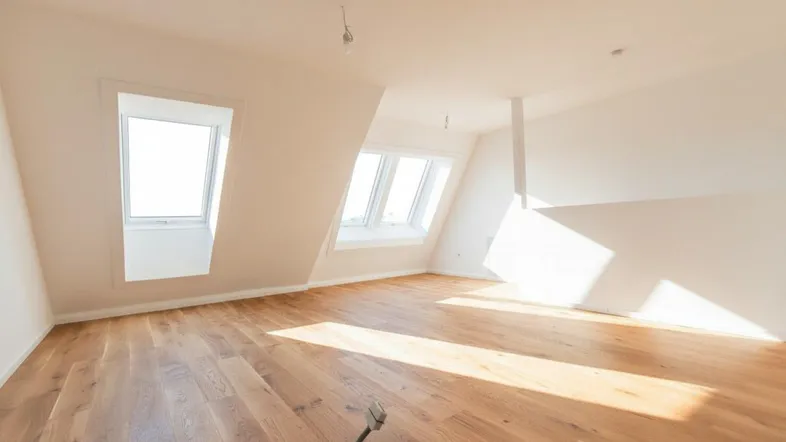 Helles, unmöbliertes Zimmer mit Dachschrägen, Holzboden und Dachfenstern.