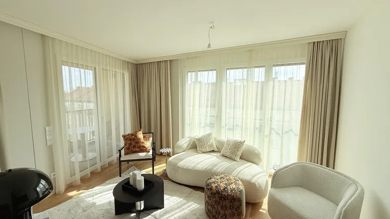 Helles Wohnzimmer mit modernem Sofa, Parkettboden und großen Fenstern zum Balkon.