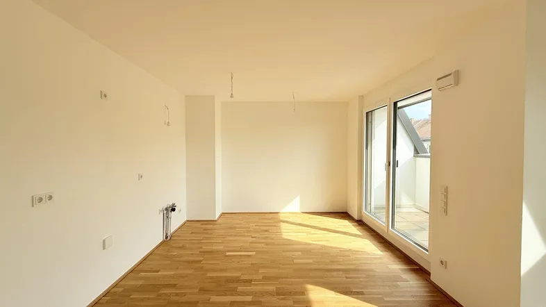 Helles, leeres Zimmer mit Parkettboden und Zugang zu einem kleinen Balkon, ideal für individuelle Gestaltung.