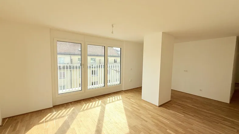 Helles, leeres Wohnzimmer mit Parkettboden und Zugang zu einem französischen Balkon.