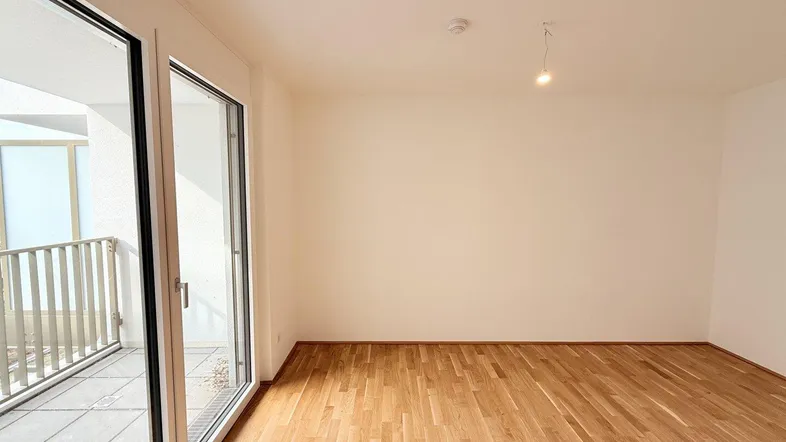 Heller Raum mit Parkettboden und Zugang zu einem Balkon, ideal als Wohnzimmer.
