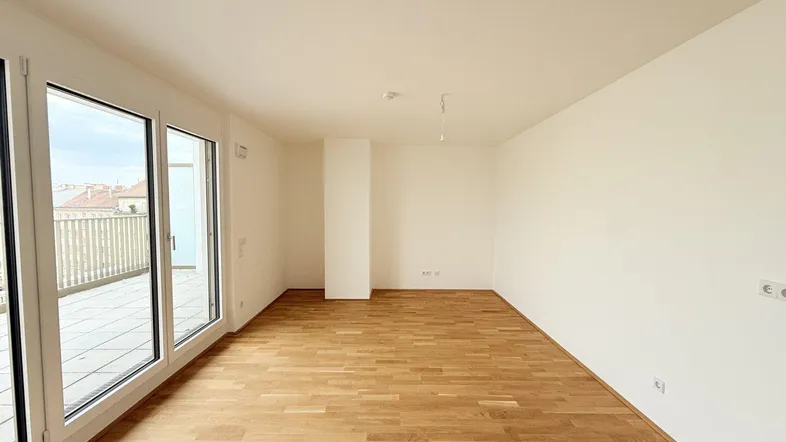 Helles, leeres Zimmer mit Parkettboden und Zugang zu einer großen Terrasse.