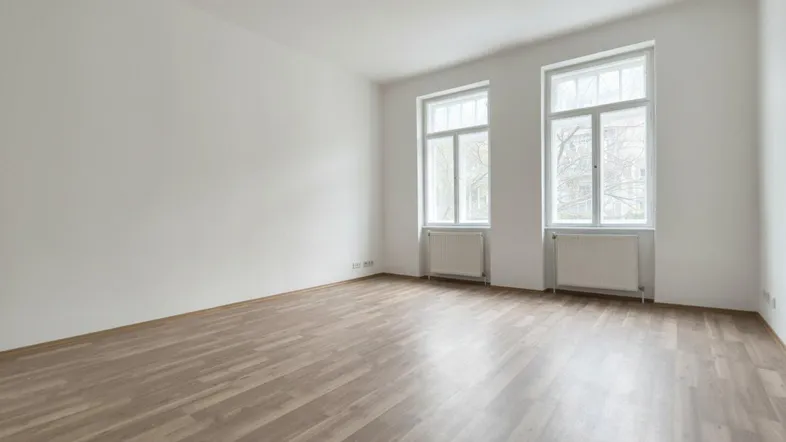 Helles, leeres Zimmer mit weiß gestrichenen Wänden und modernem Laminatboden, bereit zur individuellen Gestaltung.