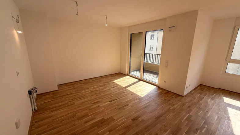 Helles Wohnzimmer mit Parkettboden und Zugang zu einem Balkon, durchflutet von Sonnenlicht.