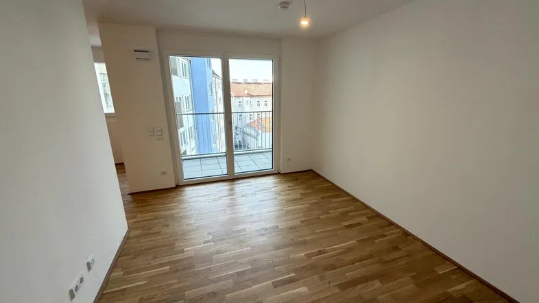 Helles Wohnzimmer mit Parkettboden, weißen Wänden und Zugang zu einem Balkon.