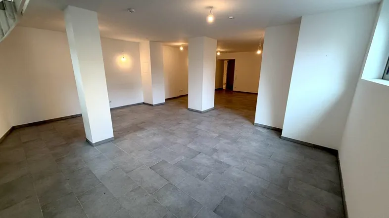Großer, leerer Raum mit grauen Fliesen und tragenden Säulen, bereit für den Ausbau.