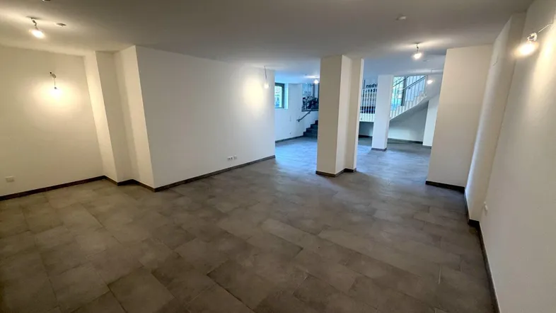Heller, geräumiger Eingangsbereich mit modernen Fliesen und Säulen, der zu einem Treppenhaus führt.