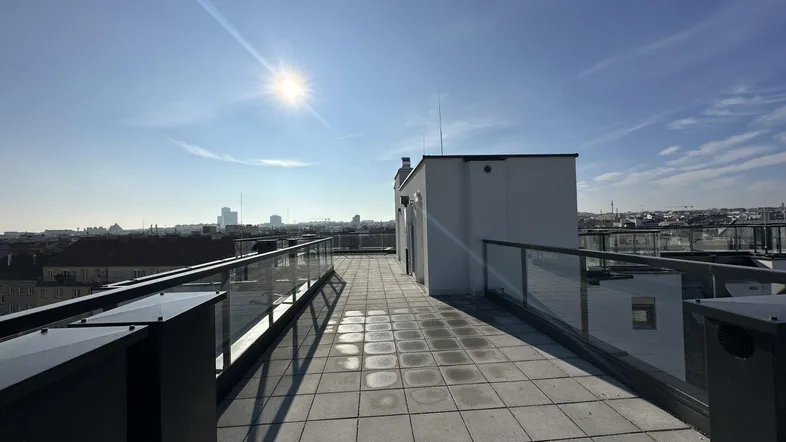 Sonnige Dachterrasse mit modernen Glasgeländern und weitem Blick über die Stadt.