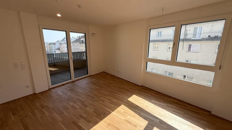 Helles Wohnzimmer mit Parkettboden, großen Fenstern und Zugang zu einem Balkon.