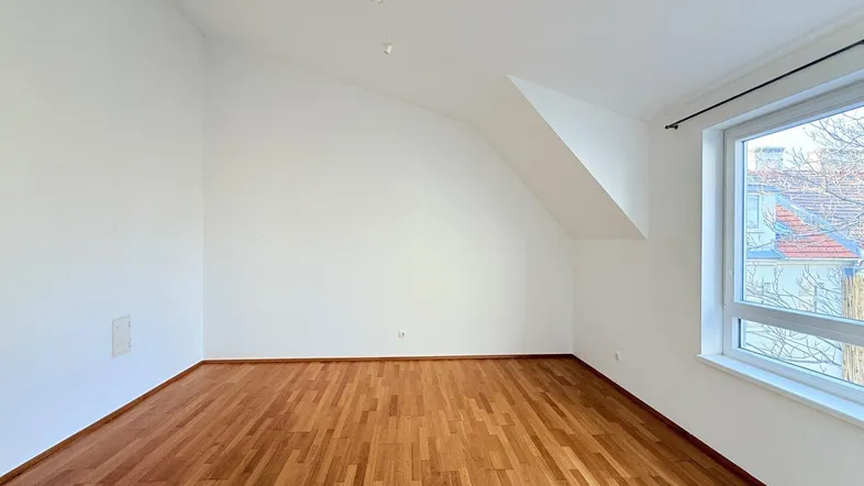 Helles Zimmer mit Parkettboden, weißen Wänden und schräger Decke, ideal als Wohn- oder Schlafbereich.