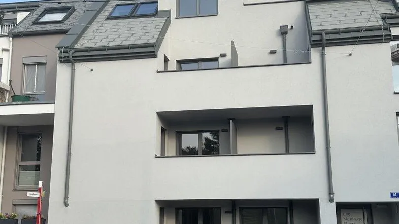 Moderne Fassade eines Mehrfamilienhauses mit Balkonen und Dachfenstern unter klarem Himmel.