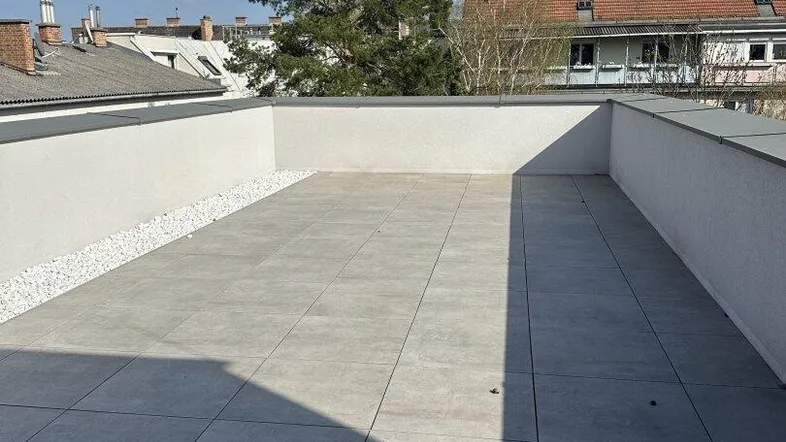 Geräumige Dachterrasse mit hellen Fliesen und Blick auf die umliegenden Dächer und Bäume.