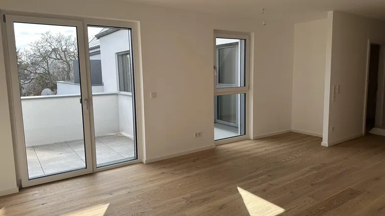 Helles Zimmer mit Holzboden und Zugang zu einem Balkon, ideal als Wohn- oder Schlafbereich.