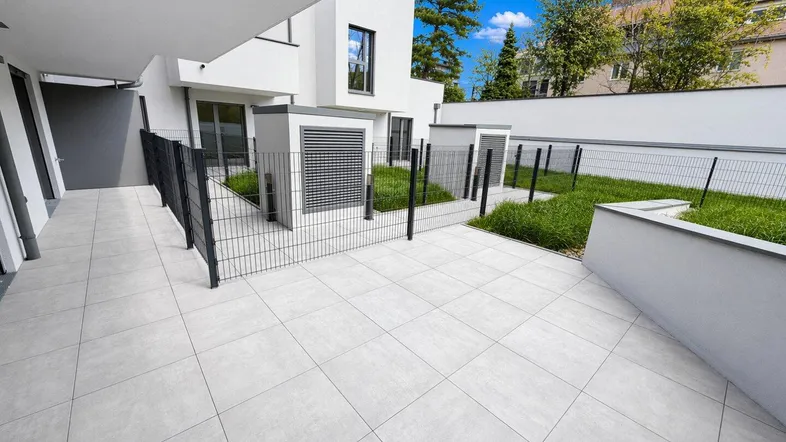 Große, modern geflieste Terrasse mit angrenzenden Grünflächen und Blick auf das Gebäude.