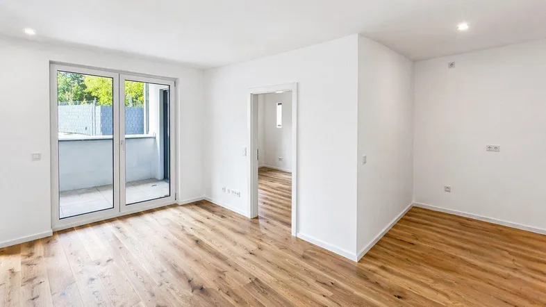 Helles, leeres Zimmer mit Holzboden und Zugang zu einem Balkon, ideal für Wohn- oder Schlafbereich.