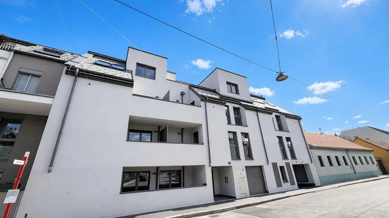 Modernes Mehrfamilienhaus mit weißer Fassade und Balkonen unter blauem Himmel an einem sonnigen Tag.