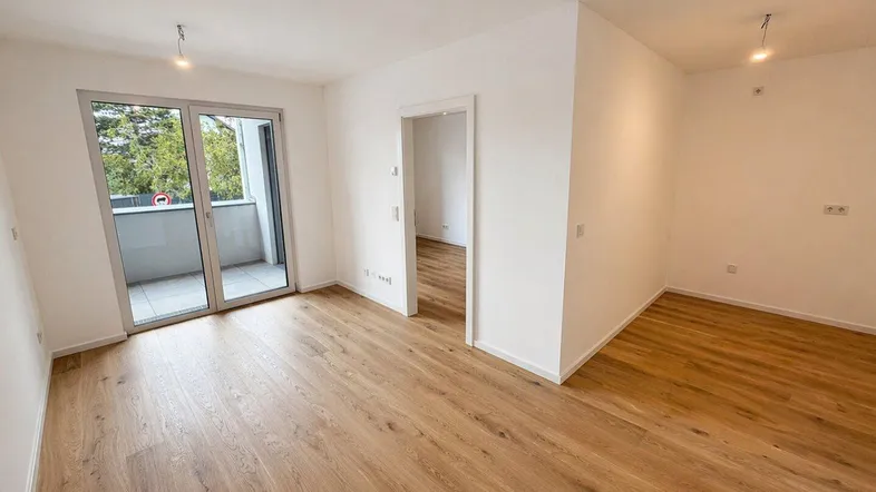 Heller Wohnraum mit modernem Laminatboden und direktem Zugang zum Balkon.