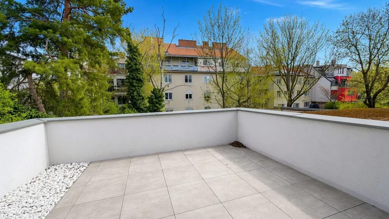Geräumige Dachterrasse mit Fliesenboden und Blick auf die umliegende Wohnbebauung und Bäume.