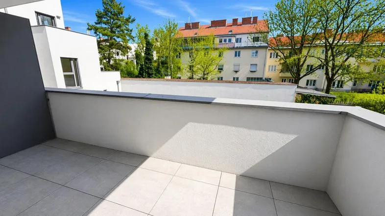 Heller Balkon mit Fliesenboden und Blick auf die umliegenden Gebäude und Bäume.