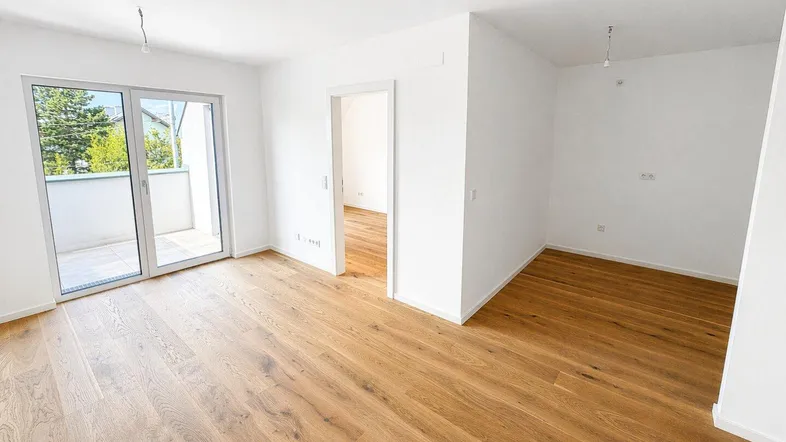 Heller Wohnraum mit neuem Parkettboden und Zugang zu einem Balkon, ideal für modernes Wohnen.