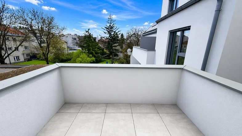 Heller Balkon mit Fliesenboden und Blick auf die umliegende Bebauung und Bäume.