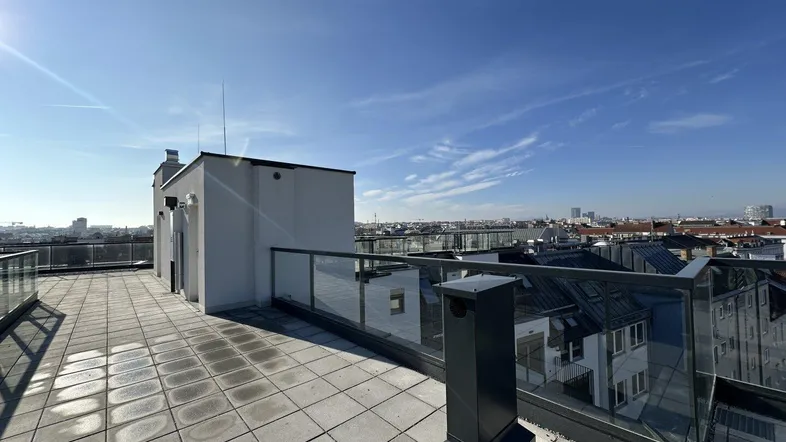 Geräumige Dachterrasse mit Fliesenboden und Glasgeländer, bietet einen weiten Blick über die Stadt.