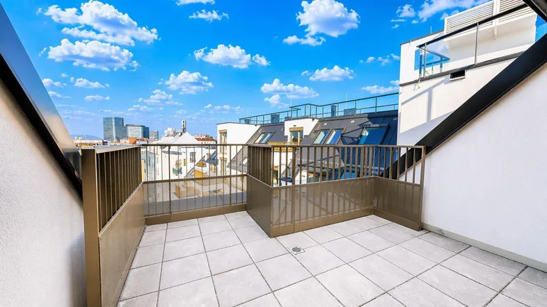 Geräumige Dachterrasse mit Fliesenboden und Blick auf die Stadt unter blauem Himmel.