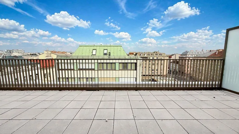 Geräumige Dachterrasse mit Fliesenboden und weitem Blick über die Stadt unter blauem Himmel.