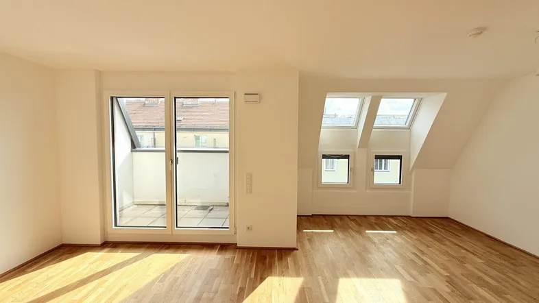Helles, leeres Zimmer mit Parkettboden, Dachschrägen und Zugang zu einem kleinen Balkon.