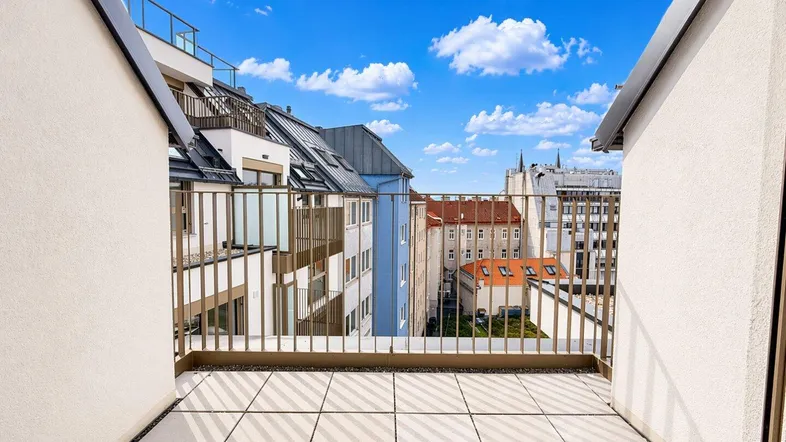 Geräumiger Balkon mit Fliesenboden und Blick auf die umliegende Stadtlandschaft unter blauem Himmel.